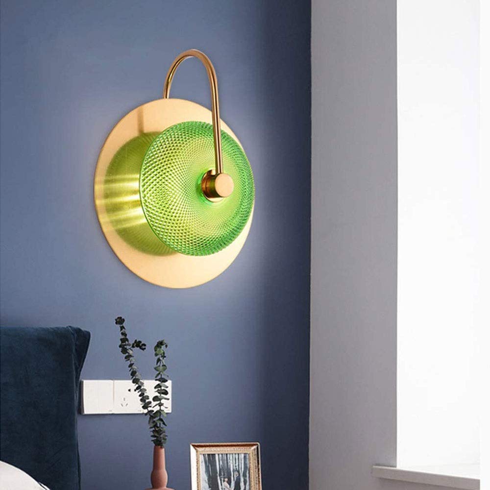 Modern wall lamp with green glass shade and gold metal fixture on a blue wall.