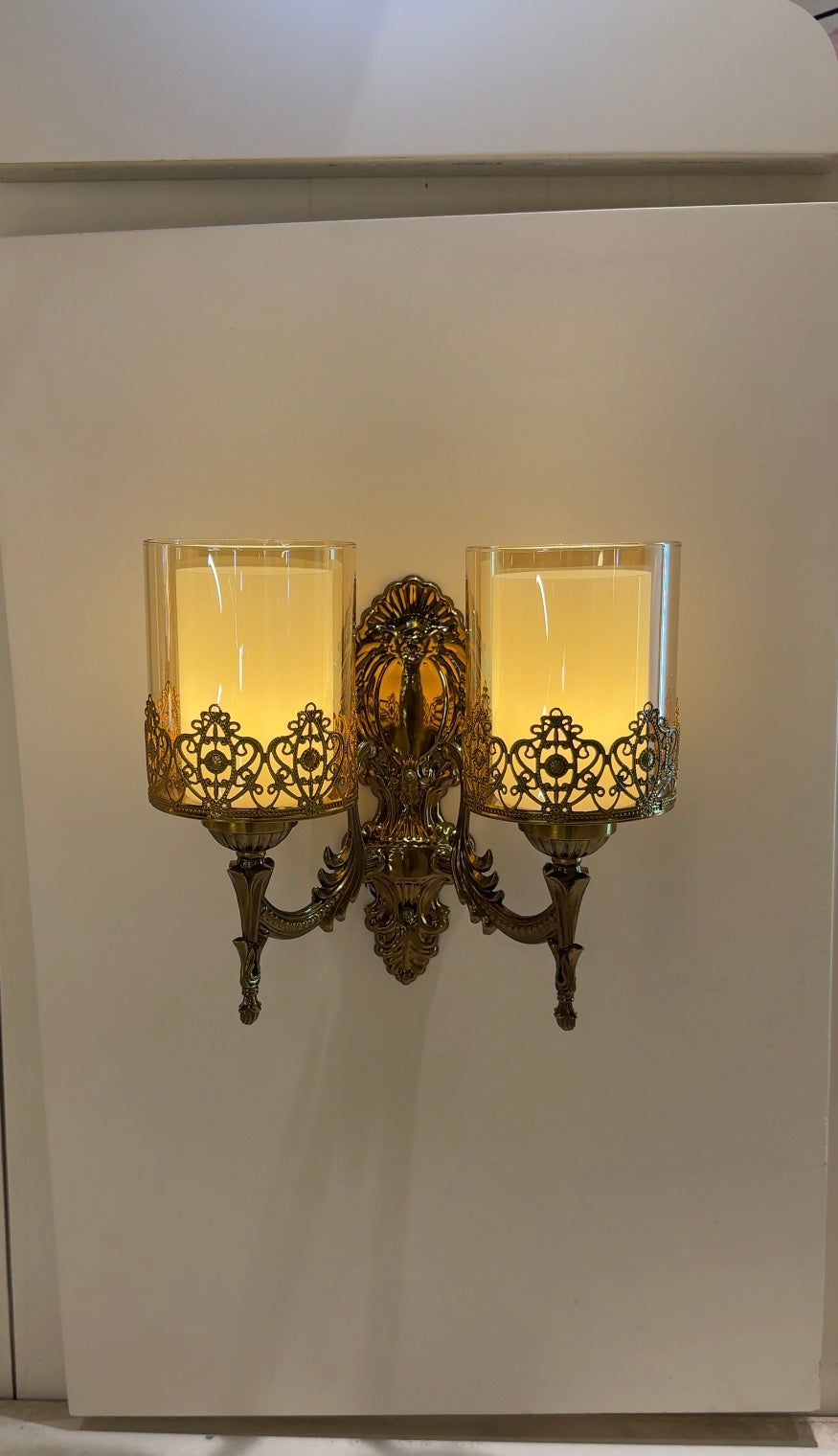 Decorative wall sconce with two lit candle-style lights on a white wall.