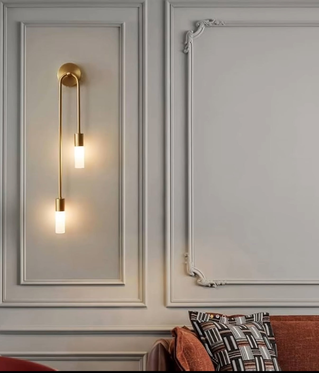 Decorative wall sconces on a wall with molding and a sofa in the background