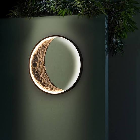 Moon-shaped wall light fixture on a green wall with plants above