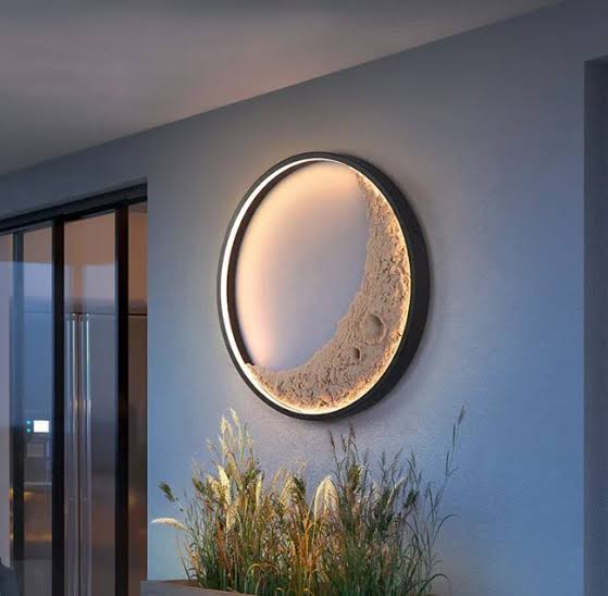 Modern wall-mounted light fixture on a gray wall with plants in the foreground