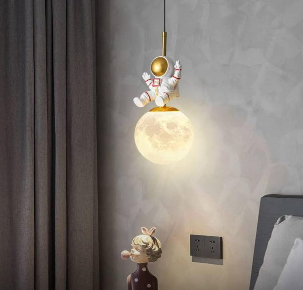 Pendant light with astronaut design on a wall, next to a child figurine.