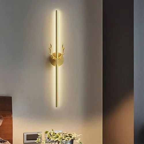 Gold wall-mounted light fixture with deer antlers on a gray wall.