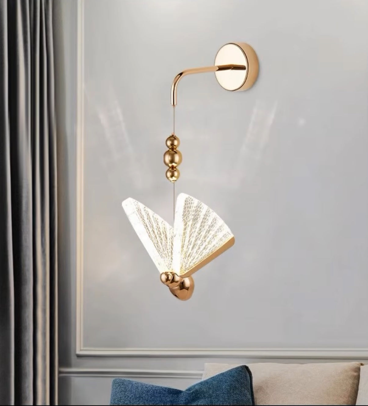 Gold wall-mounted lamp with decorative design on a light gray wall.