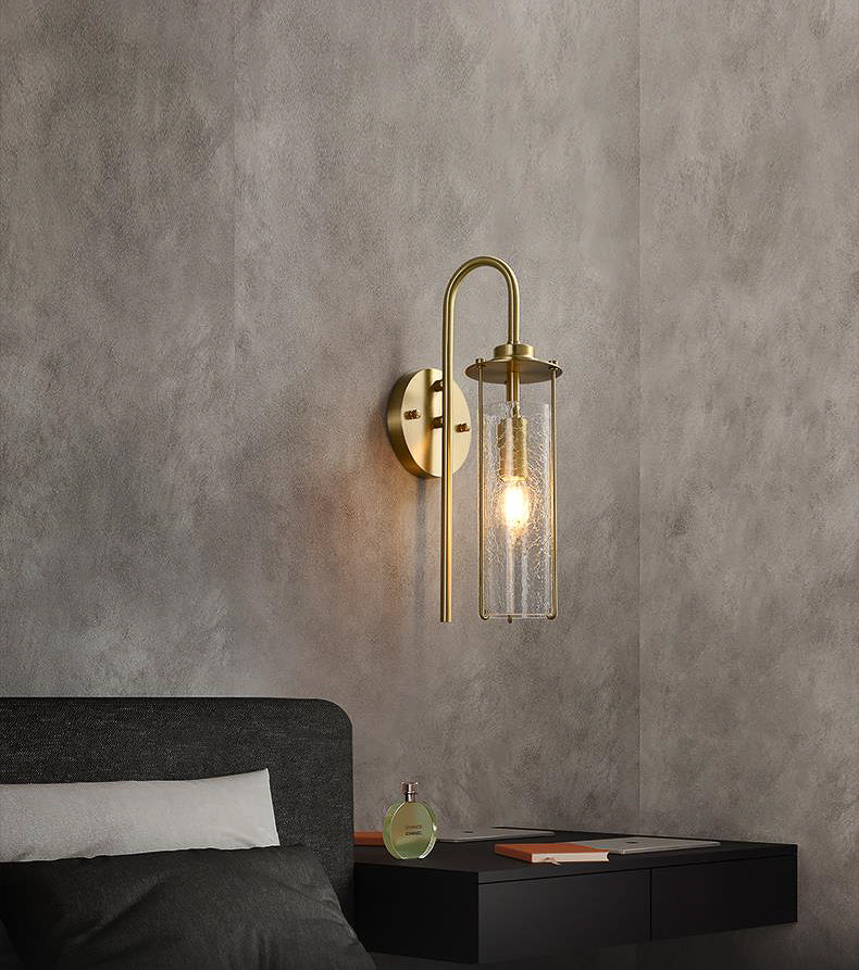 Gold wall sconce with glass shade on a gray wall above a bed.