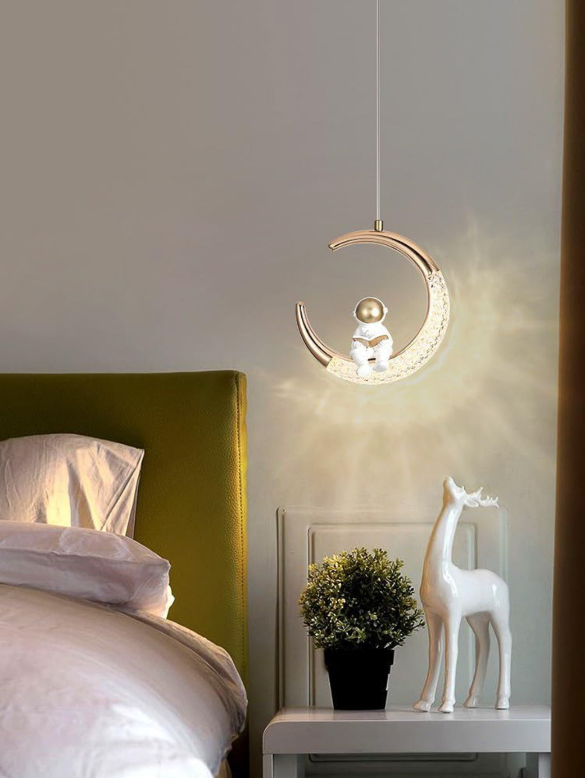 Decorative pendant light hanging above a bed with a nightstand featuring a plant and deer figurine.