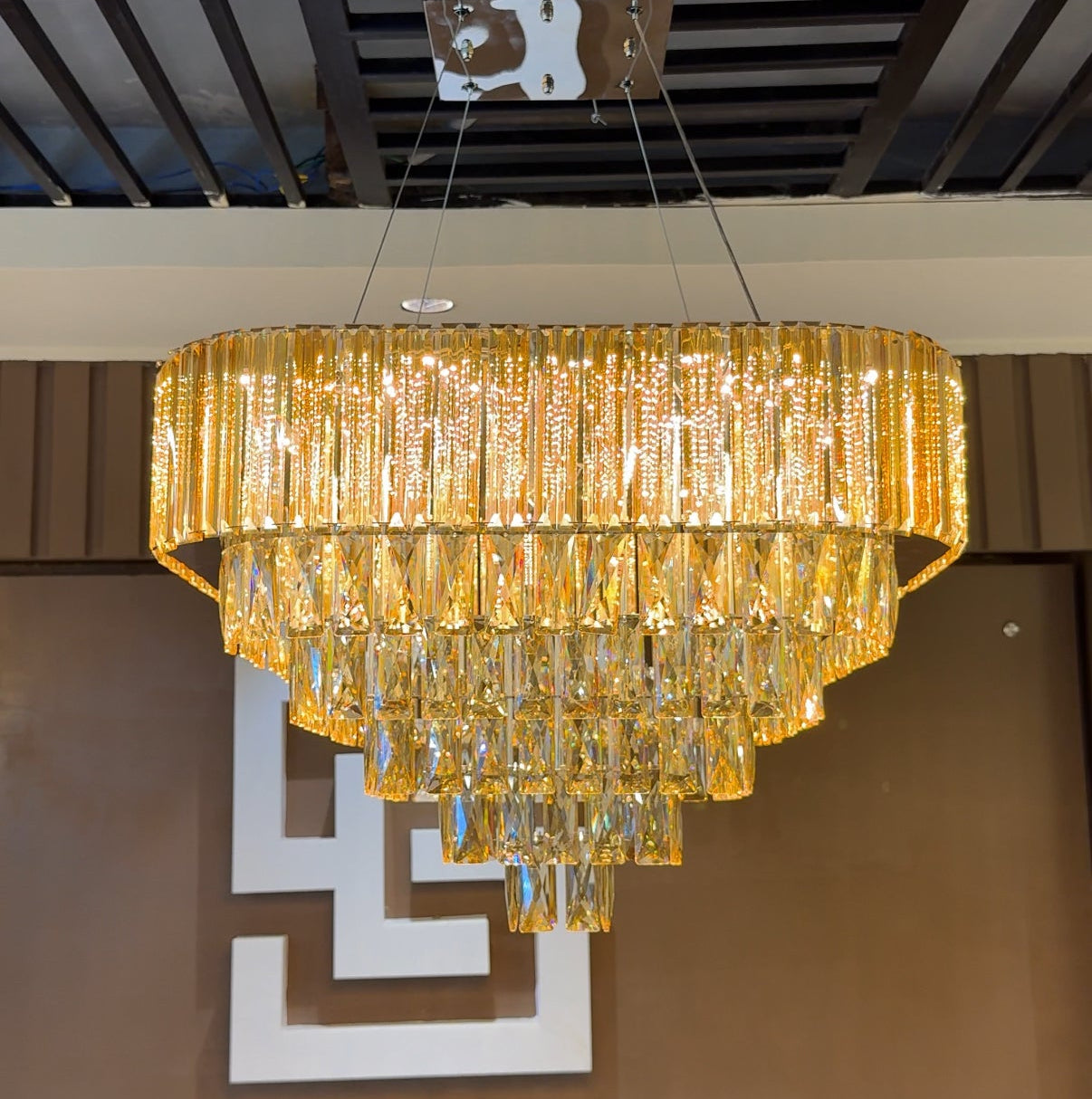 Gold chandelier hanging from a ceiling with a brown wall and decorative elements in the background