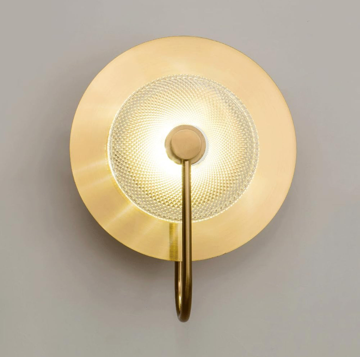 Gold wall sconce with a textured glass shade on a gray background