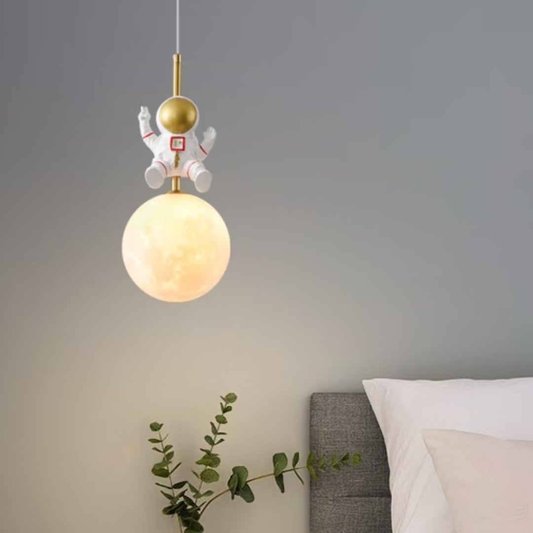 Pendant light with astronaut design hanging in a room with a plant and bed in the background.