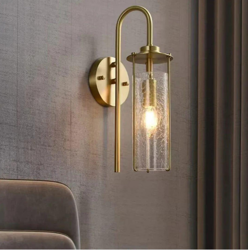 Gold wall sconce with clear glass shade on a gray wall.