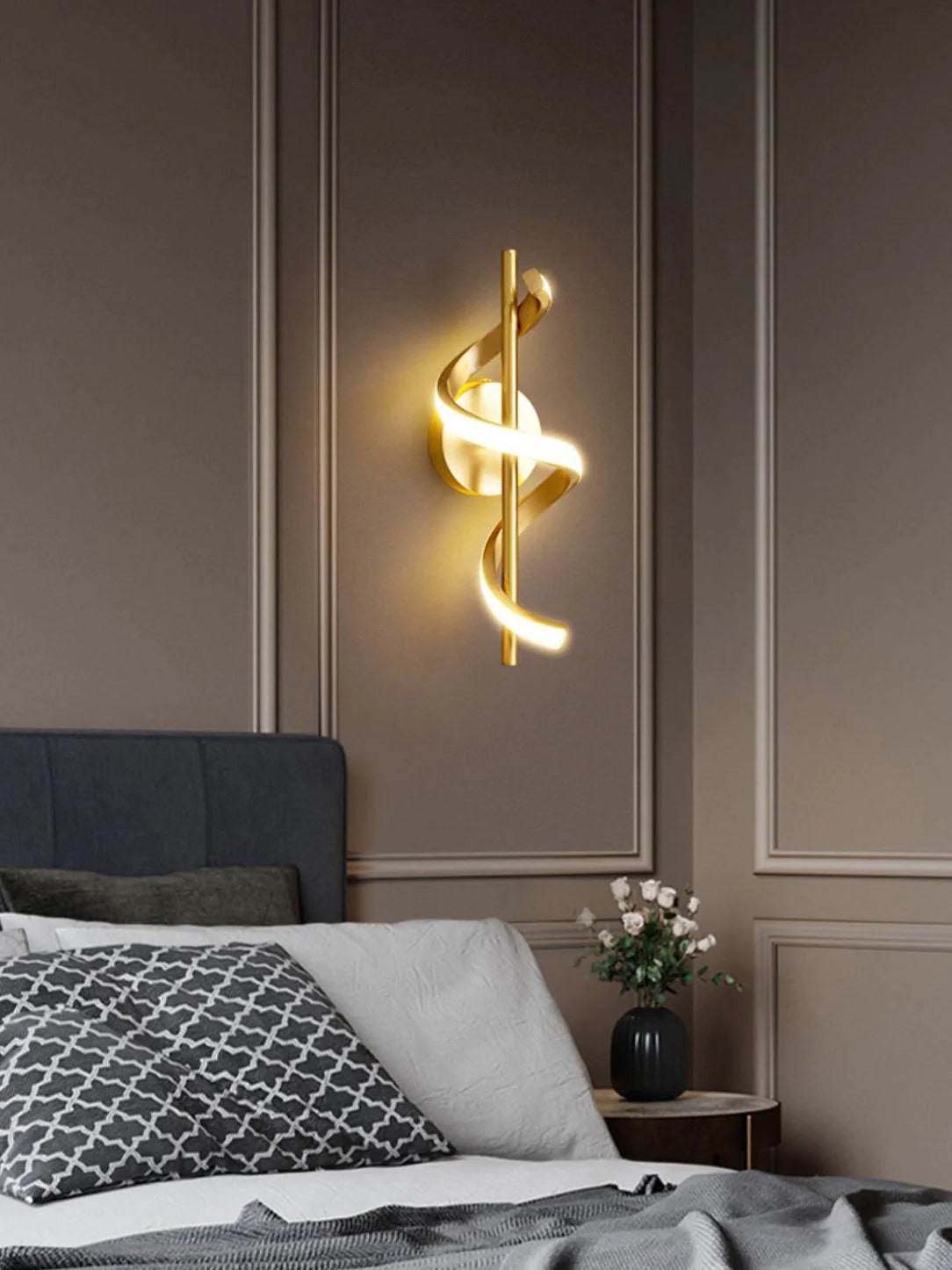 Decorative wall light fixture on a wall above a bed with pillows and a vase.