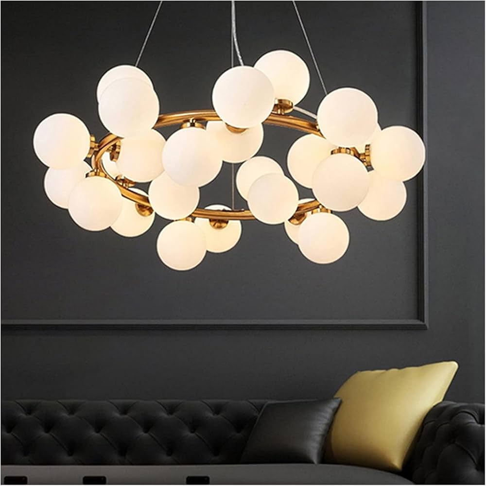 Modern chandelier with multiple light bulbs hanging above a black sofa with a yellow pillow.