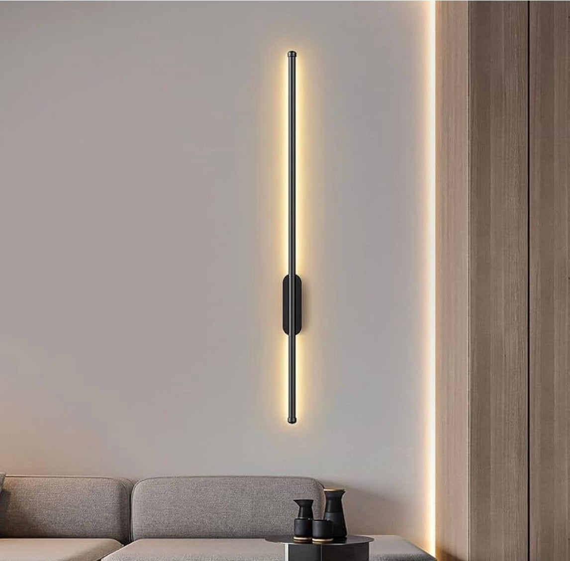 Modern wall-mounted light fixture on a neutral wall with a sofa and decorative items in the foreground.