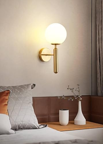 Modern wall sconce with a round light fixture on a neutral wall above a bed.