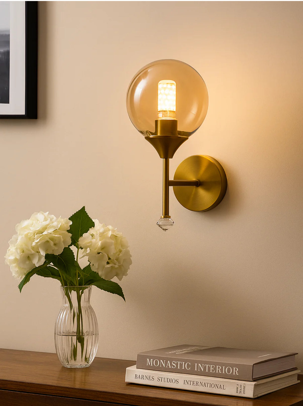 Gold wall sconce with a light bulb, vase of flowers, and books on a wooden surface.
