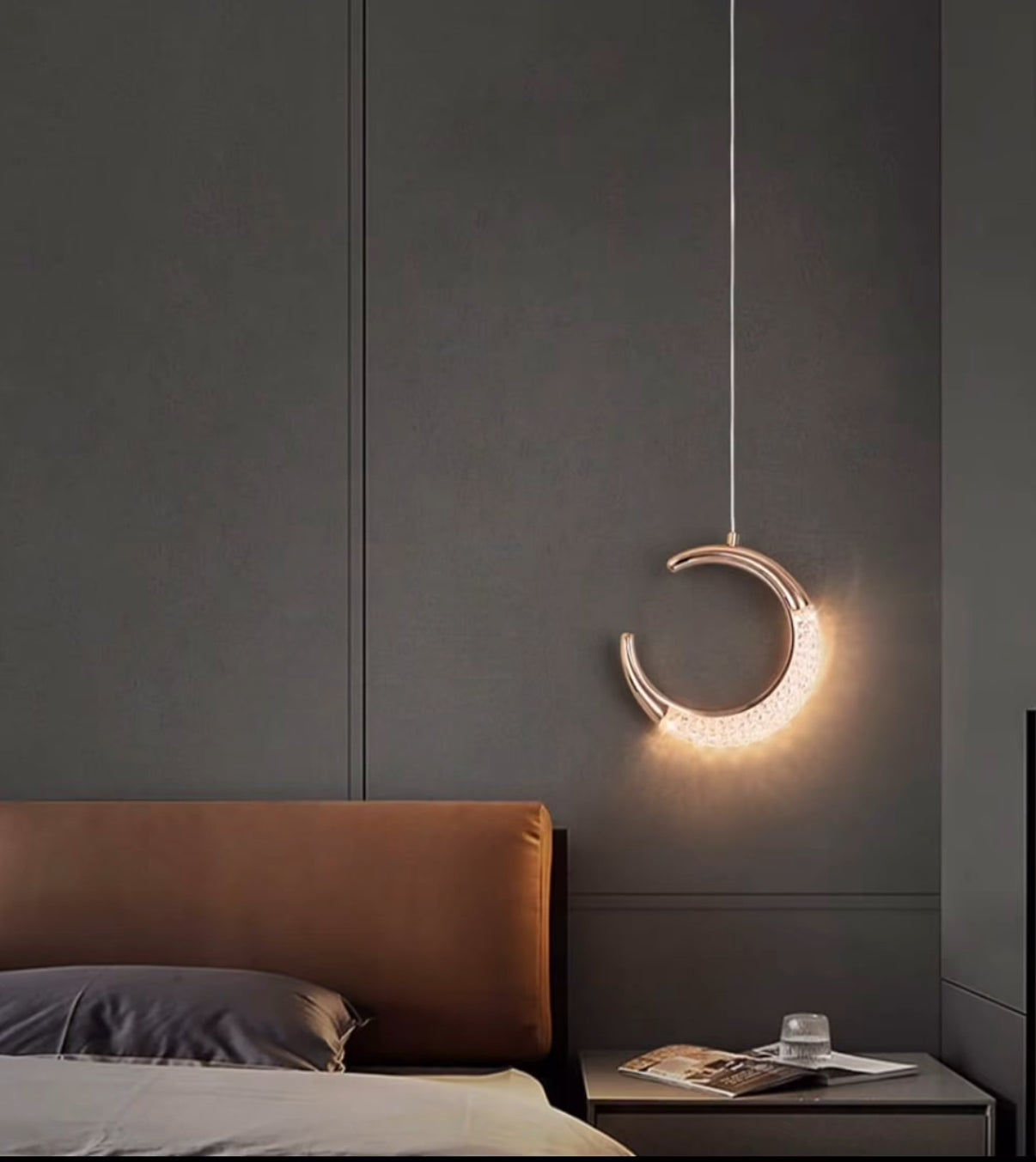 Modern pendant light shaped like a crescent moon in a bedroom setting.