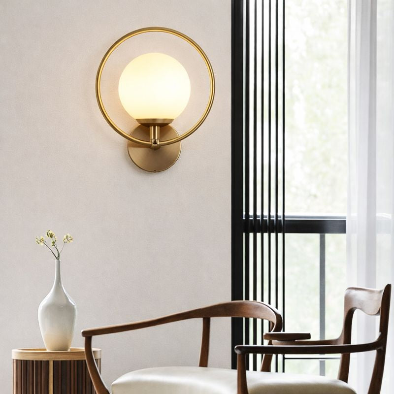 Modern wall lamp with a round glass shade in a room with chairs and a vase.