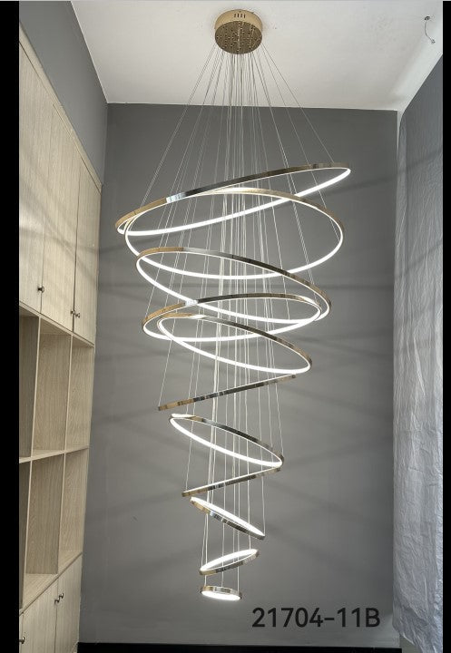 Modern spiral chandelier hanging from a ceiling in a room with gray walls and wooden shelves.