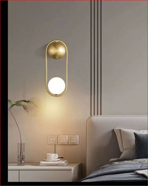 Modern wall lamp on a neutral wall with a bed and nightstand in the background