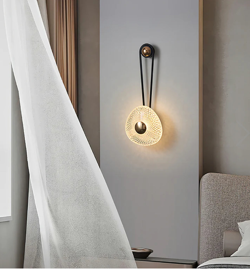 Modern wall lamp with a textured design on a neutral wall next to a curtain and sofa.