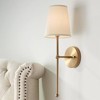 Wall sconce with beige lampshade on a white wall next to a beige sofa.