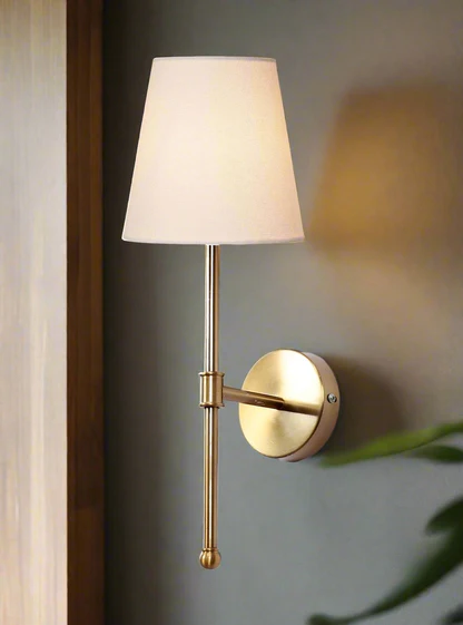 Wall-mounted lamp with a gold arm and white shade on a gray wall.
