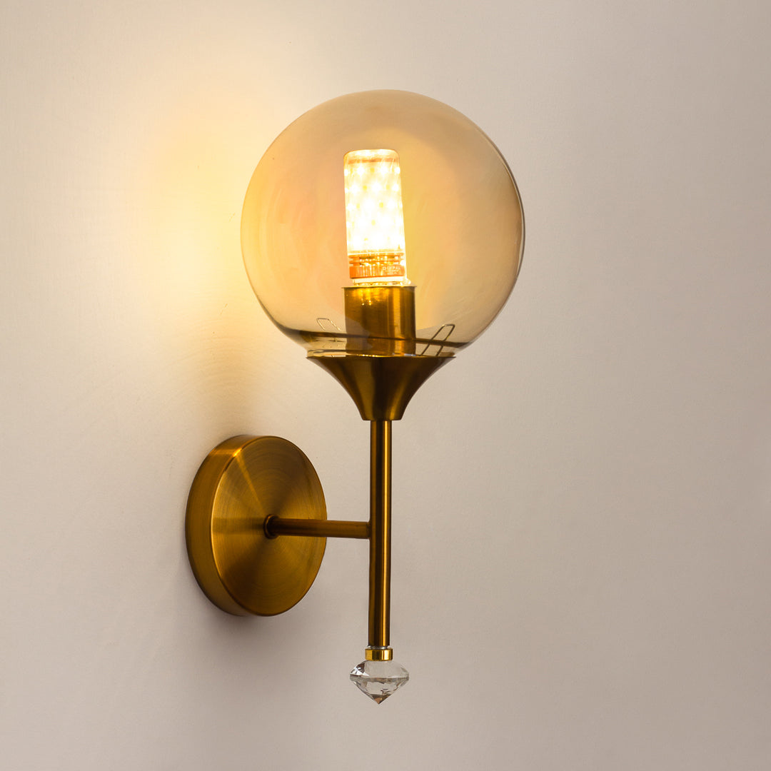 Gold wall sconce with a glass globe shade on a neutral background