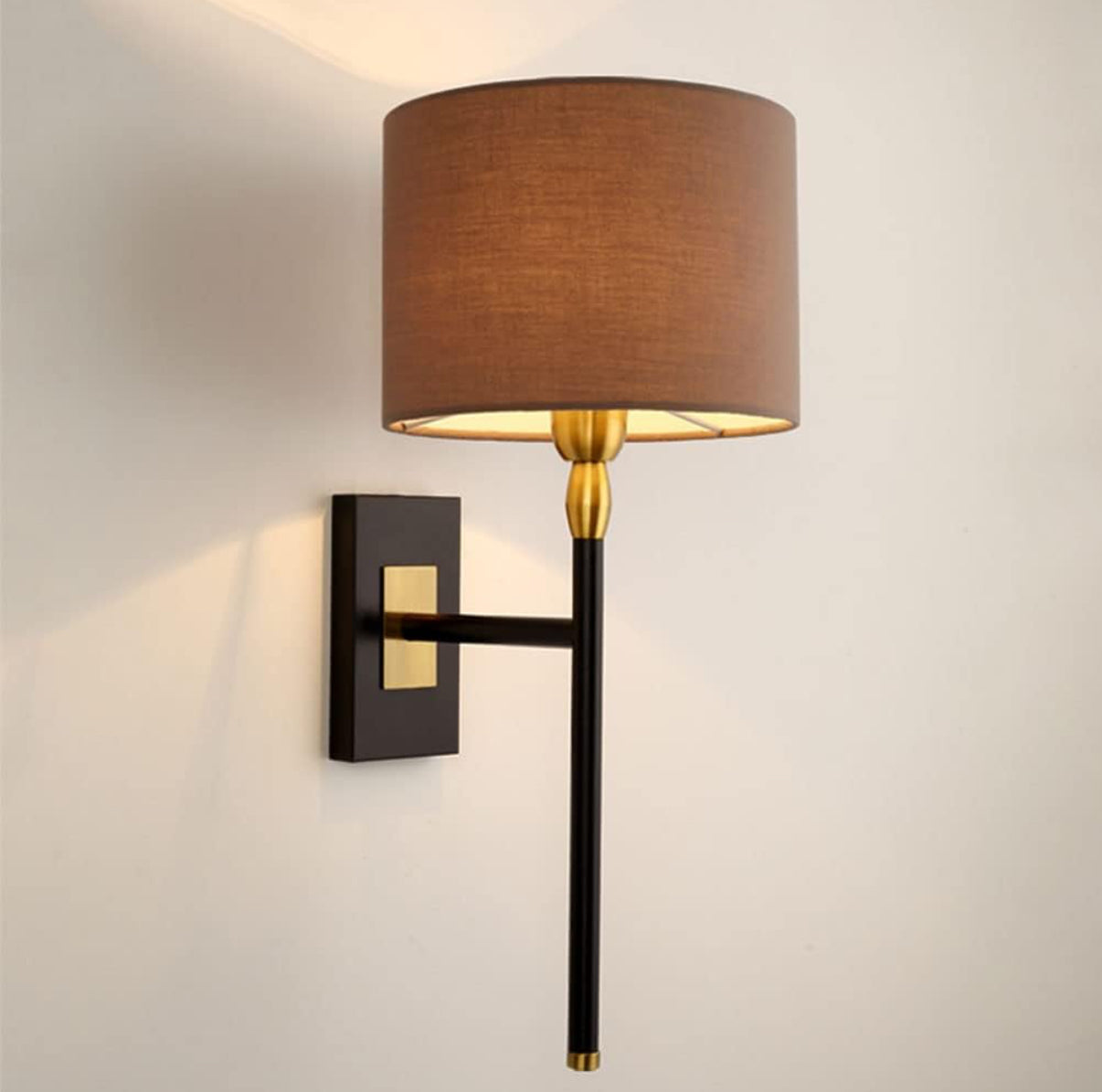Wall-mounted lamp with brown shade and black and gold arm on a light gray wall.
