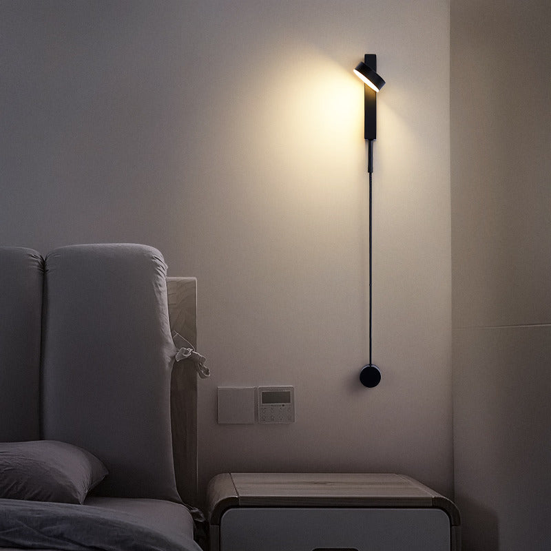 Modern wall lamp on a neutral wall next to a bed in a bedroom setting.