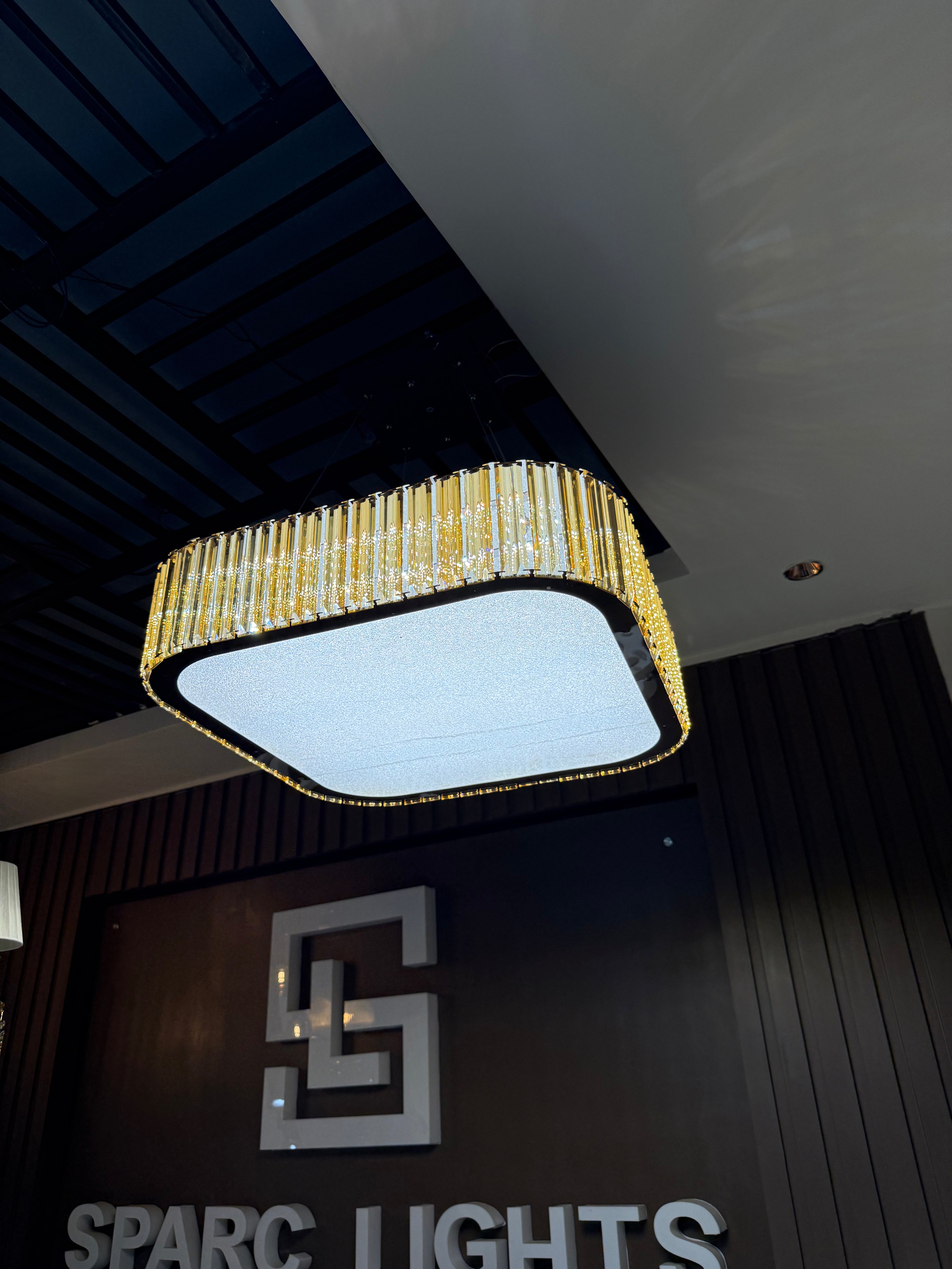 Modern chandelier hanging above a branded sign for 'Sparc Lights'.