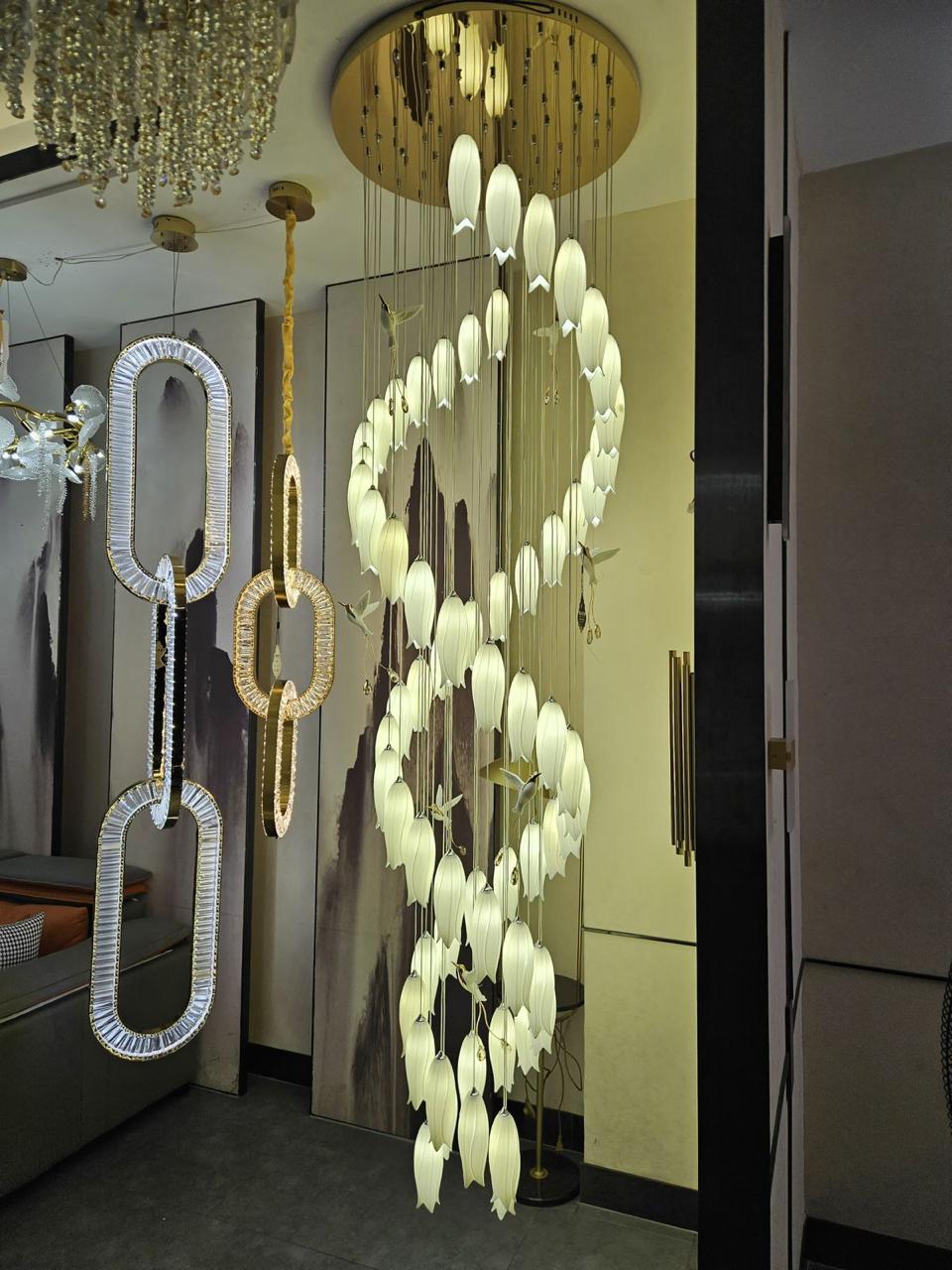 A gold-colored metal chandelier with a tulip-shaped design, featuring multiple hanging lights, displayed in a room with a mirrored wall and a luxurious décor setting.