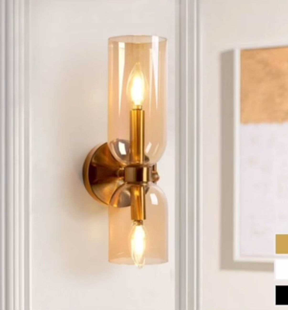 Wall-mounted lamp with gold fixture and clear glass shade on a white wall.