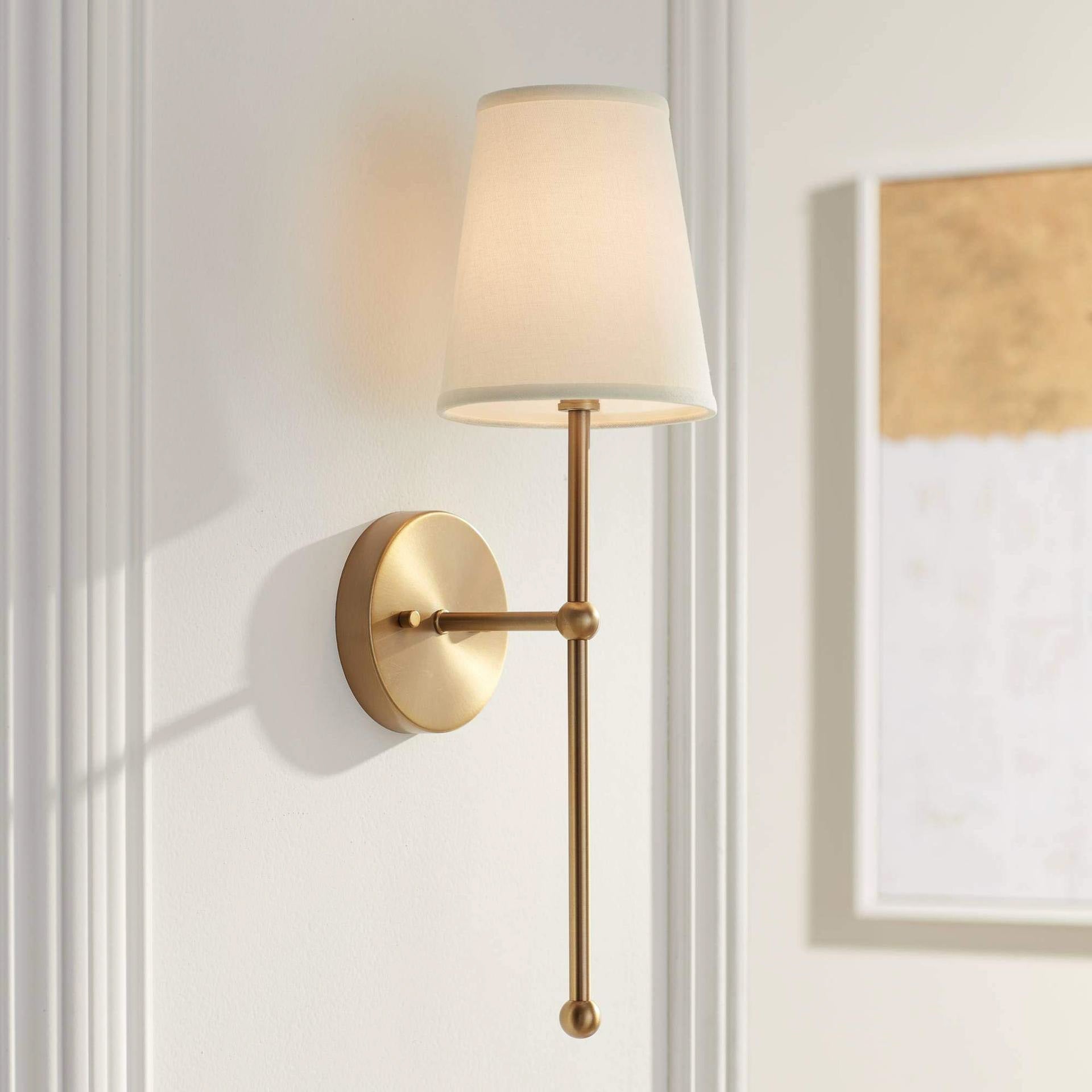 Wall-mounted lamp with gold fixture and white shade on a light gray wall.