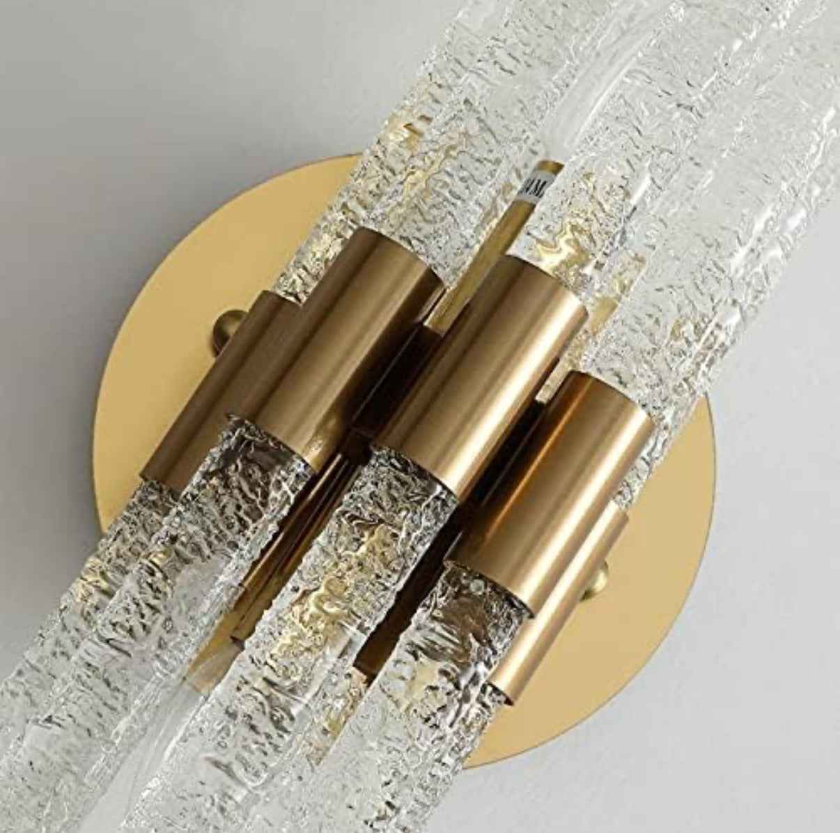 Wall-mounted light fixture with gold and crystal design on a neutral background